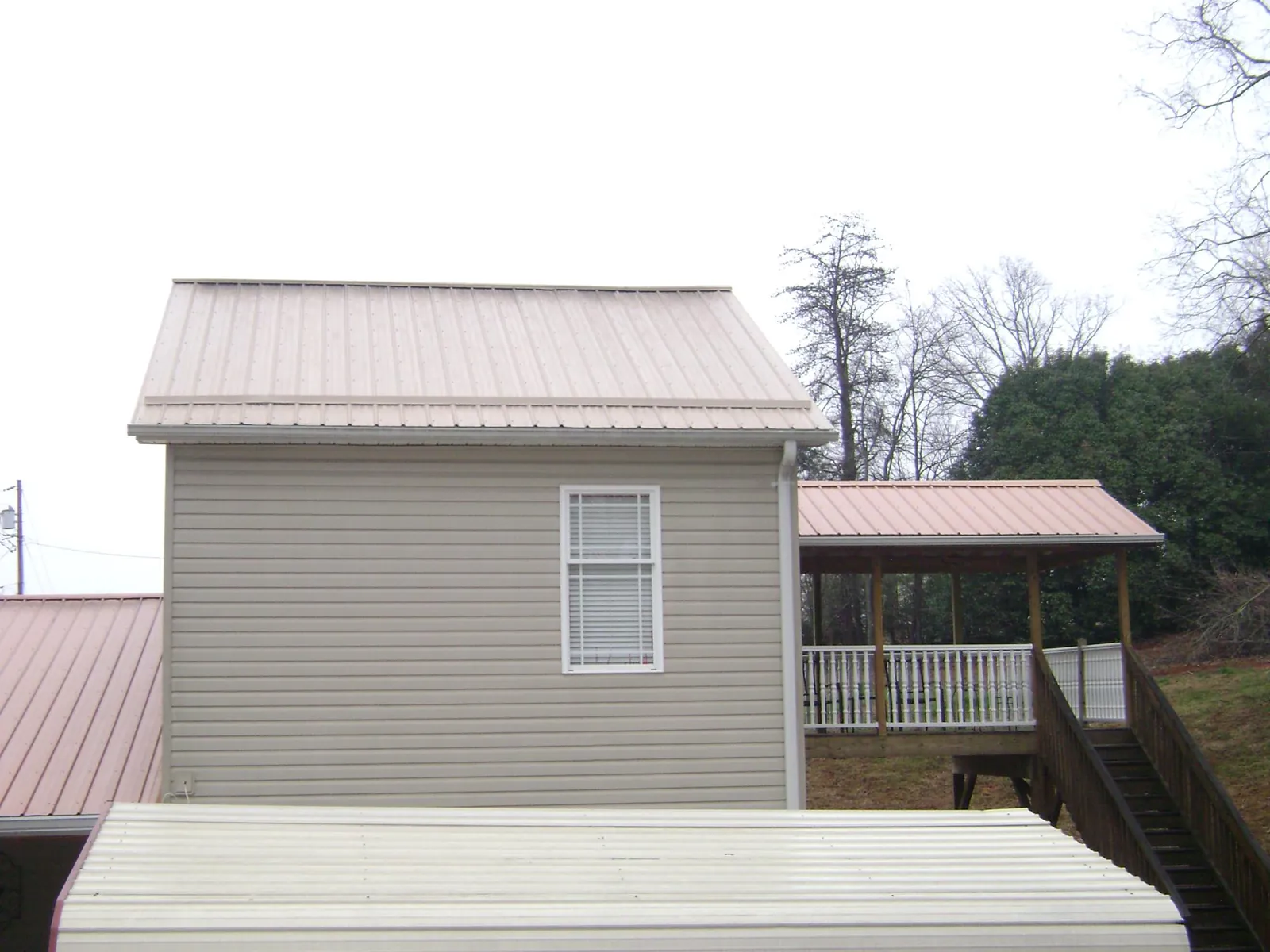 Tan metal roofs on a two story addition and attached porch, from a Roof Replacement job in Westover